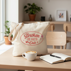Baumwollbeutel Broken Hearts Club auf Café-Tisch mit Kaffeetasse und Notizbuch