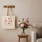 Stoffbeutel Love is all we need mit rosa Schleifen und roten Herzen hängt an Wand neben Blumen