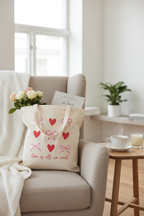 Baumwollbeutel Love is all we need gefüllt auf beigem Sessel mit Blumen und Buch neben Teetasse