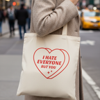 Frau trägt Statement Stoffbeutel I hate everyone but you in beigem Mantel in Stadt